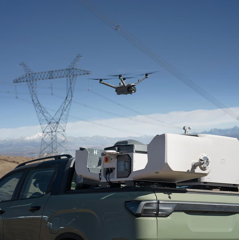 Enterprise drone flying near a power-line tower, with a ground vehicle in the foreground